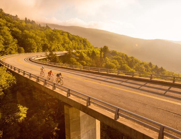 Three cyclists on the Blue Ridge Parkway's Linn Cove Viaduct, a bridge that weaves along the side of a mountain.