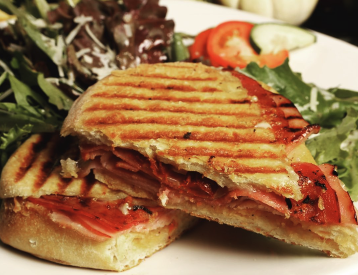 Grilled Italian panini filled with sliced meats, cheese, and roasted red peppers, served with a side salad at Pane e Vino Pizzeria in Huntsville.