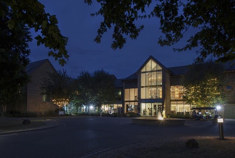 The front entrance of the De Vere Cotswold Water Park glows with warm light against a clear night sky