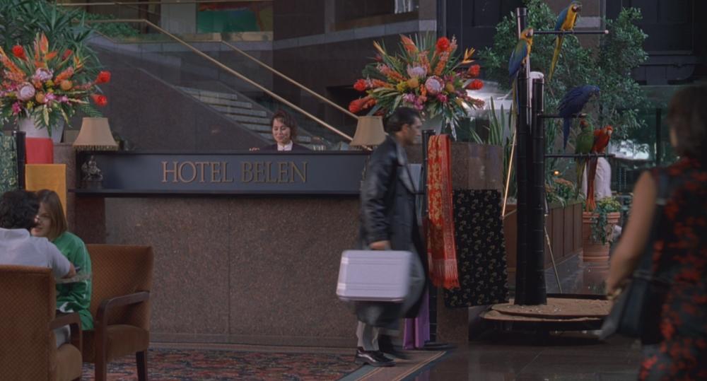 Spy Kids screengrab showing Antonio Banderas walking in front of a hotel front desk with sign reading Hotel Belen. He is wearing a leather coat and carrying a silver case