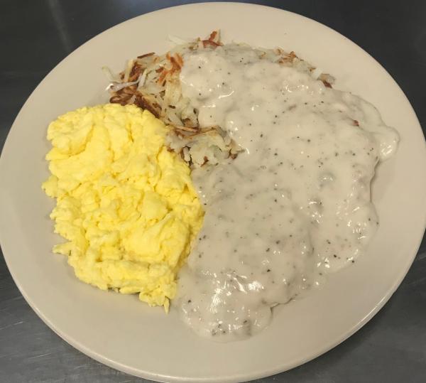 A plate of scrambled eggs with hashbrowns and breakfast meat covered in sausage gravy from and Golden Egg