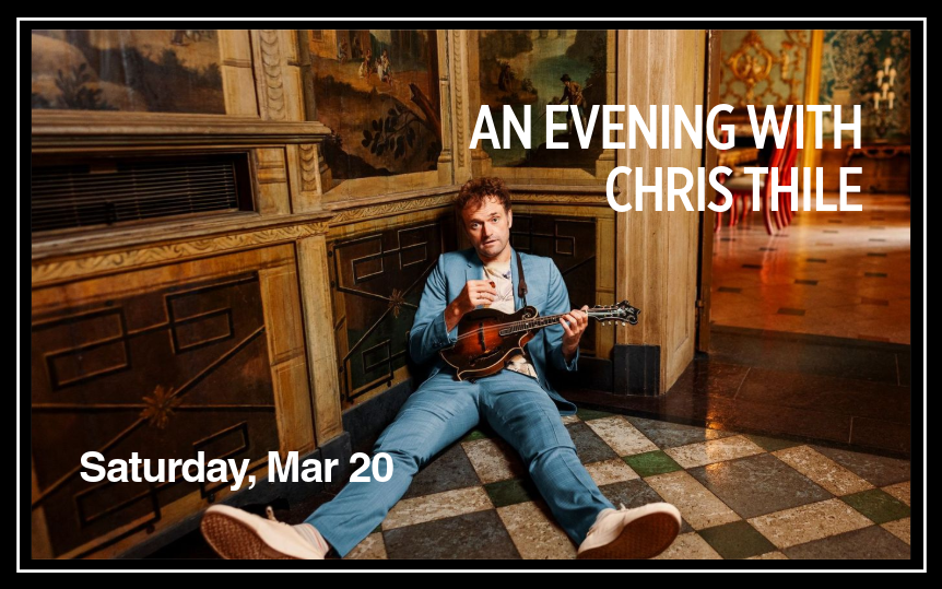 Chris Thile sits on the floor holding his mandolin