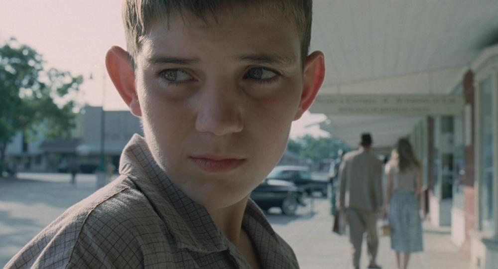 Tree of Life Screengrab showing a close-up of a young boy's face as he watches an arrest in the Town Square