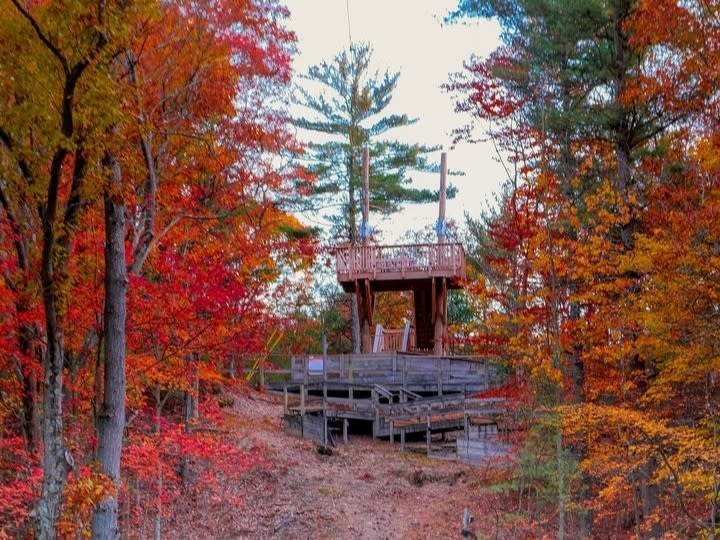A wooden deck and zipline platform surrounded by colorful autumn foliage in Muskegon State Park at the Muskegon Luge Adventure Sports Park.