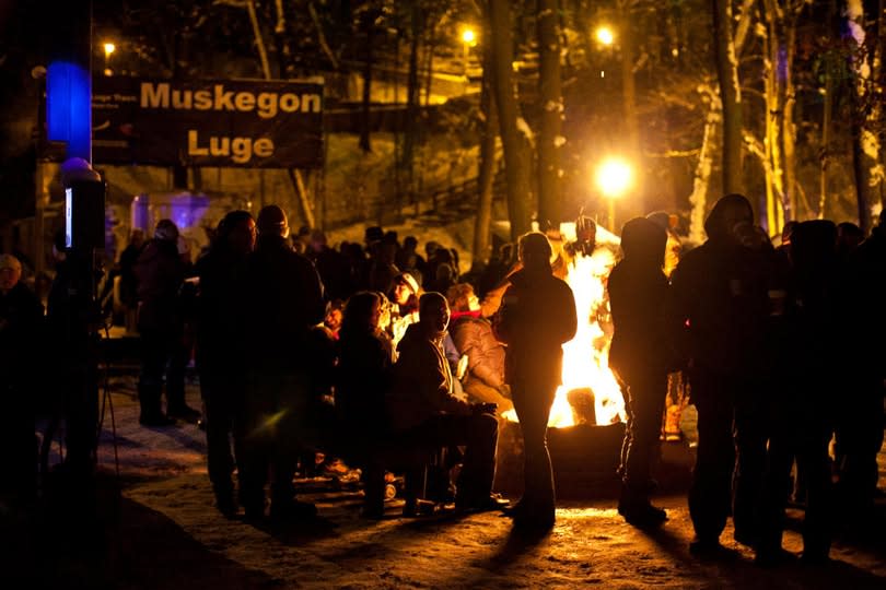 People gathered around a fire at night at the Muskegon Luge Adventure Sports Park.