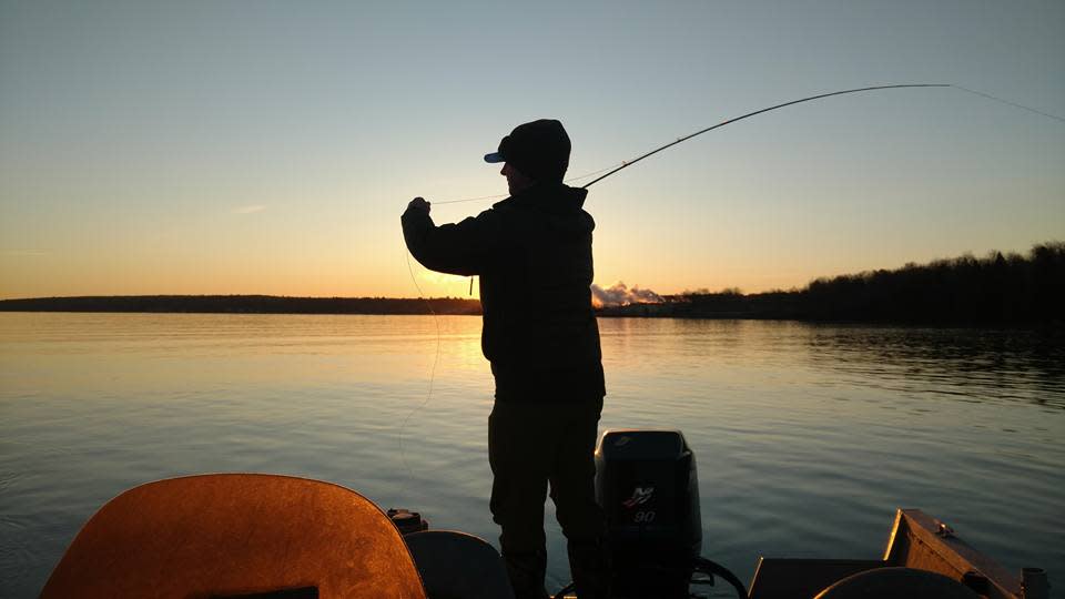 Fisherman makes a cast from boat at sunset.