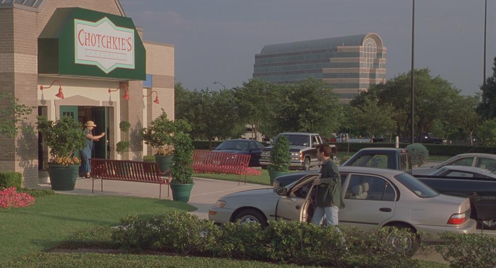 Office Space screengrab showing the exterior and green sign at Chotchkie's. A man is getting out of his car in front of the building