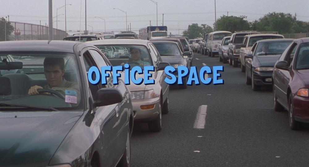 Office Space screengrab with title card reading "Office Space" in blue letters. Behind, Peter is in his car driving to work on Parmer Lane