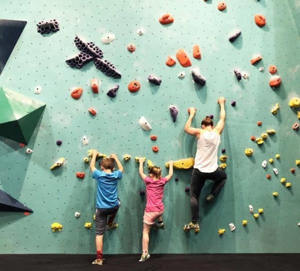 Two children and an adult female climb a rock wall at Minneapolis Bouldering Project