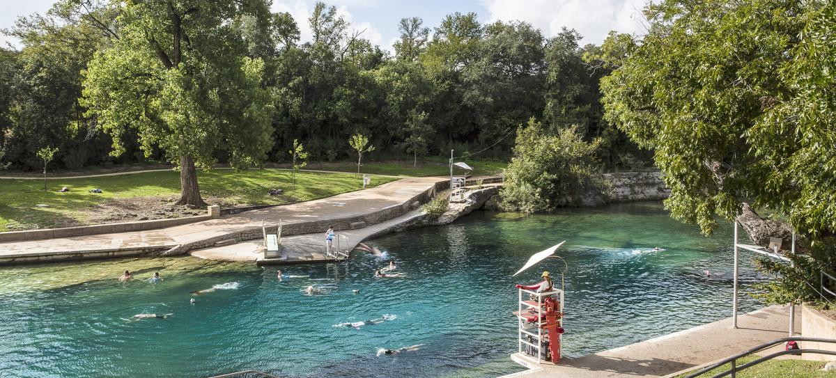 Historic Barton Springs Pool with several people swimming through the clear water and a lifeguard on duty