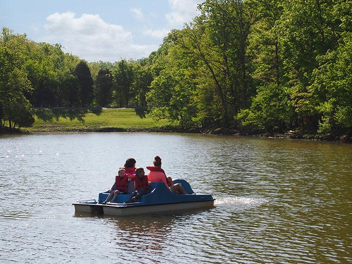Image is of a family on a paddle boat during the day, surrounded by water and tree's.