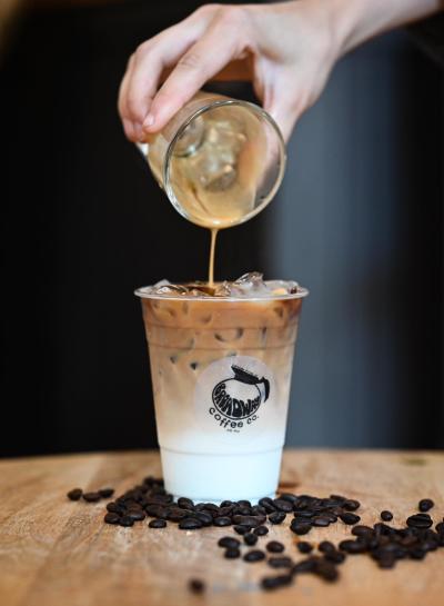 espresso being poured into a latte with coffee beans on the table