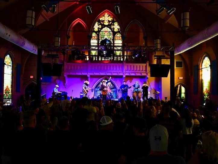 A band plays on stage in front of a large stained glass window in the sanctuary room at Southgate House Revival.