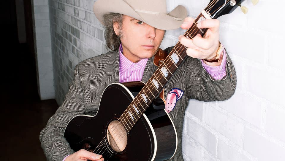 Dwight Yoakam poses for a photo wearing a cowboy hat and holding a guitar