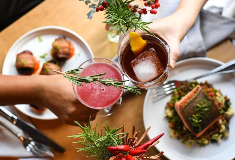 A birdseye view of two people clicking glasses over a table of food at Cardinal Spirits