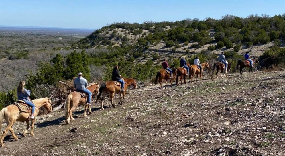 Horseback riders proceed single file along a trail at GF Ranch Trail Rides in Fredericksburg, TX