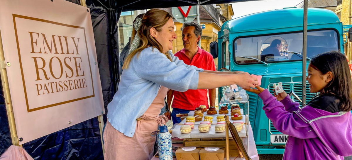 Lady handing girl a cake at a market stall