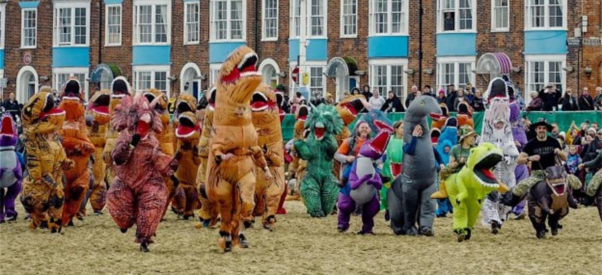Charity runners dressed up as dinosaurs running along the sand at Weymouth Beach in Dorset