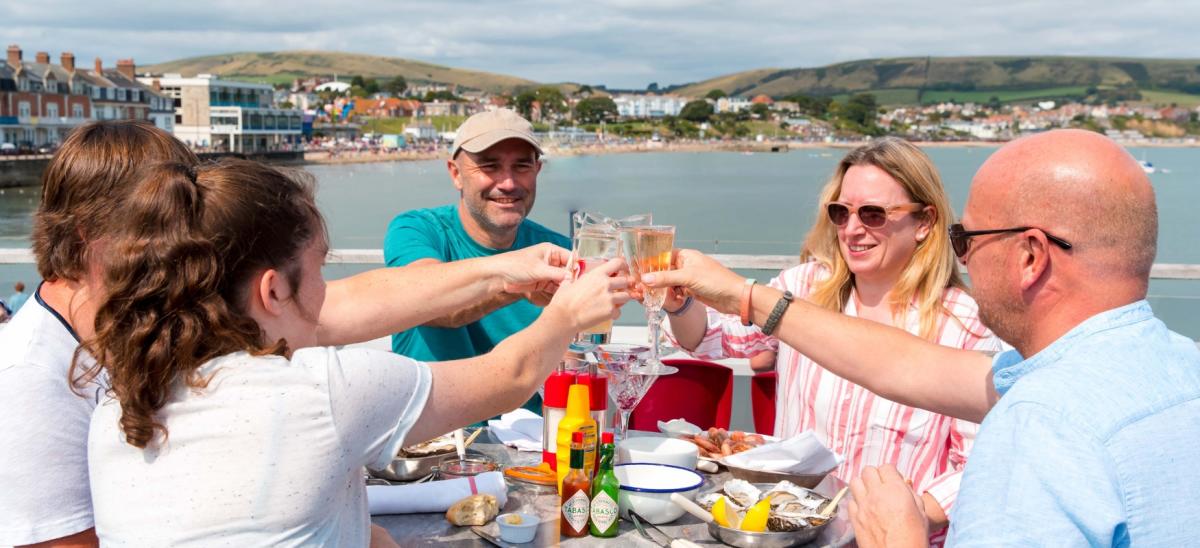 5 people eating on the top deck at Gee Whites restaurant in Swanage overlooking Swanage Bay.