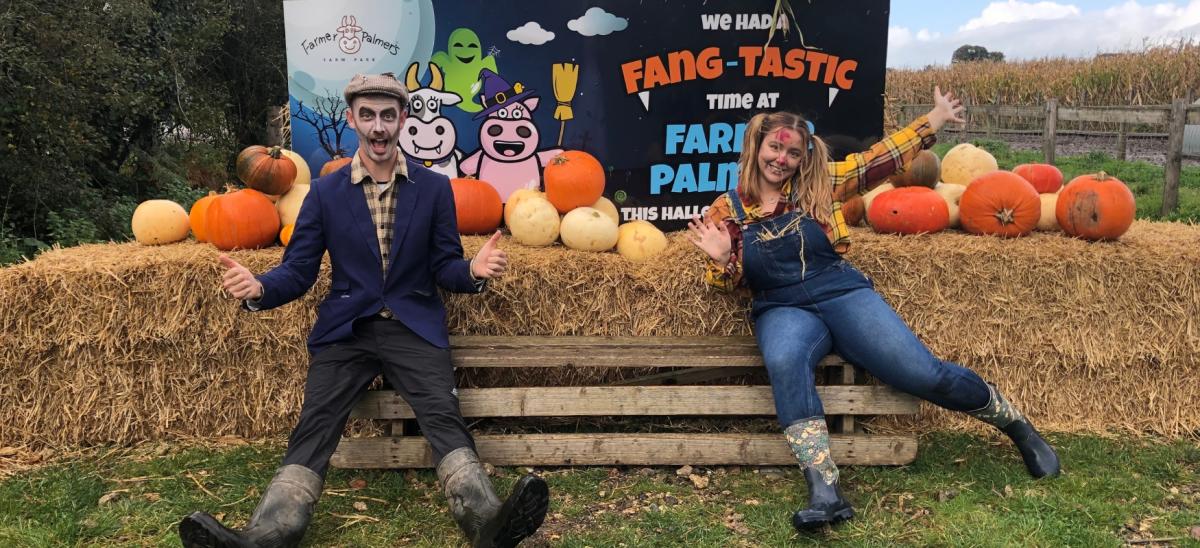 Two people dressed in Halloween fancy dress sitting next to hay bales and pumpkins at Farmer Palmers Farm Park in Dorset