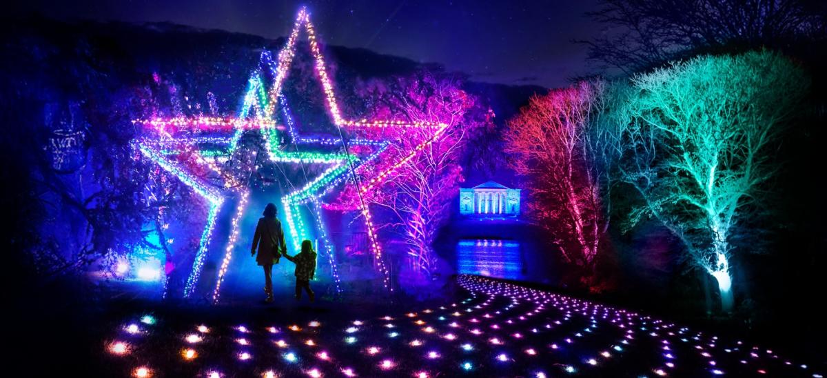 Two people walking through giant, colourful illuminated stars in the grounds of Stourhead in Wiltshire during winter