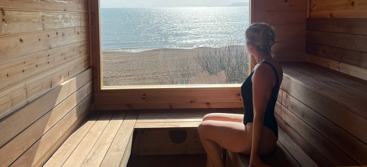 Image of a woman in a sauna, looking out through a window at the sea