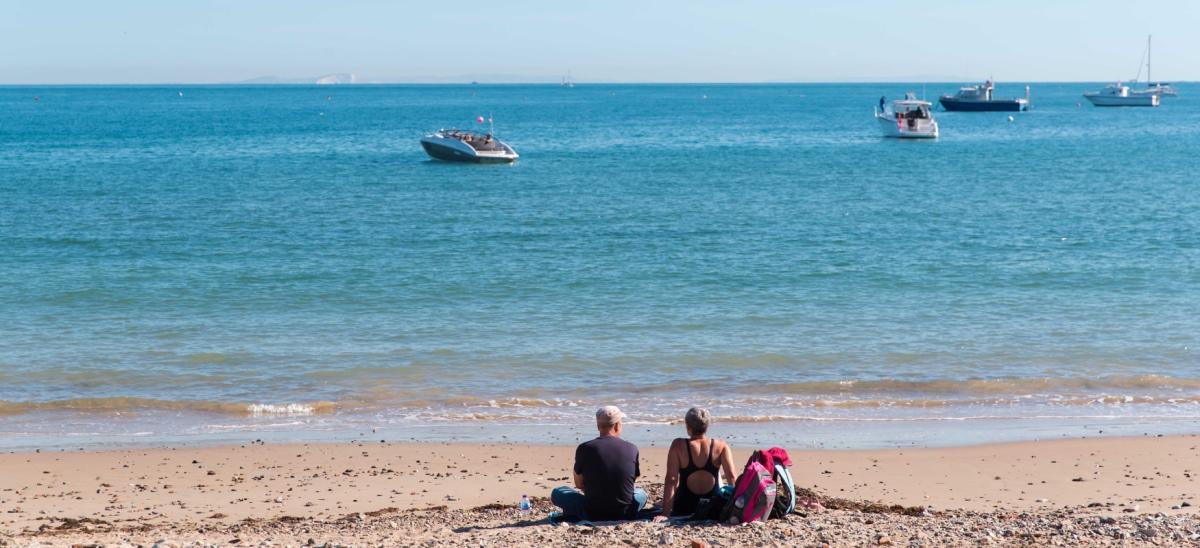 A man and woman sitting on Swanage Beach during the summer
