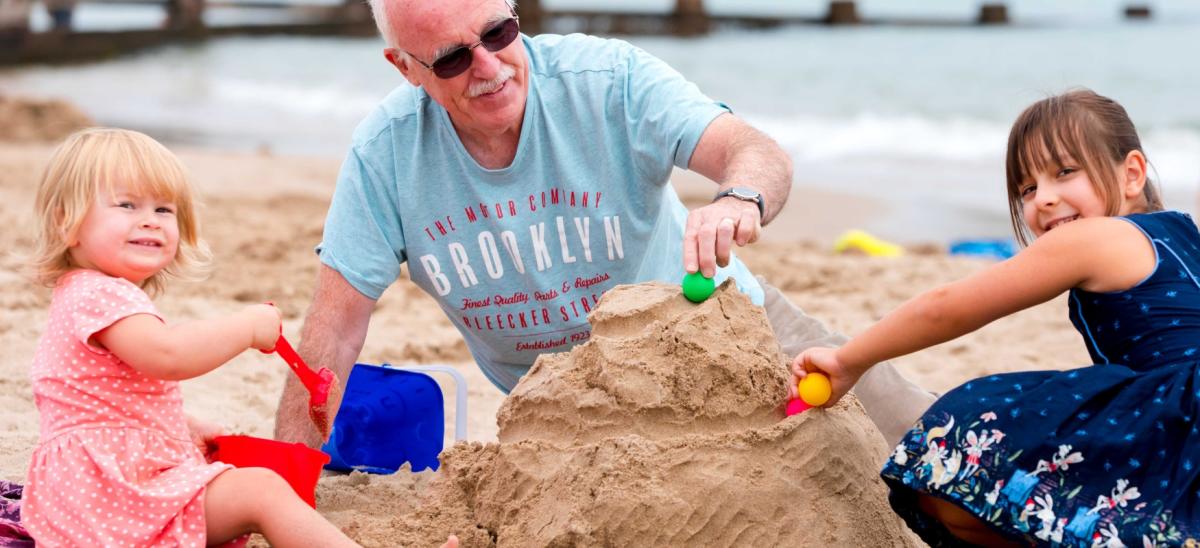 Two young girls and their grandad building sandcastles on Swanage Beach in Dorset
