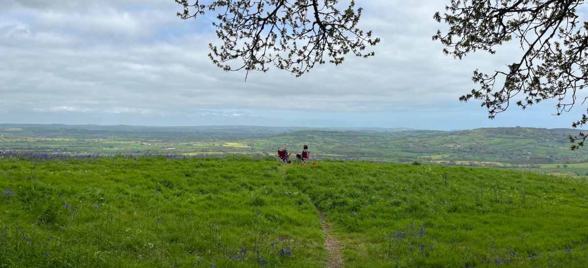 Image shows two ladies in camping chairs overlooking sweeping countryside views in West Dorset