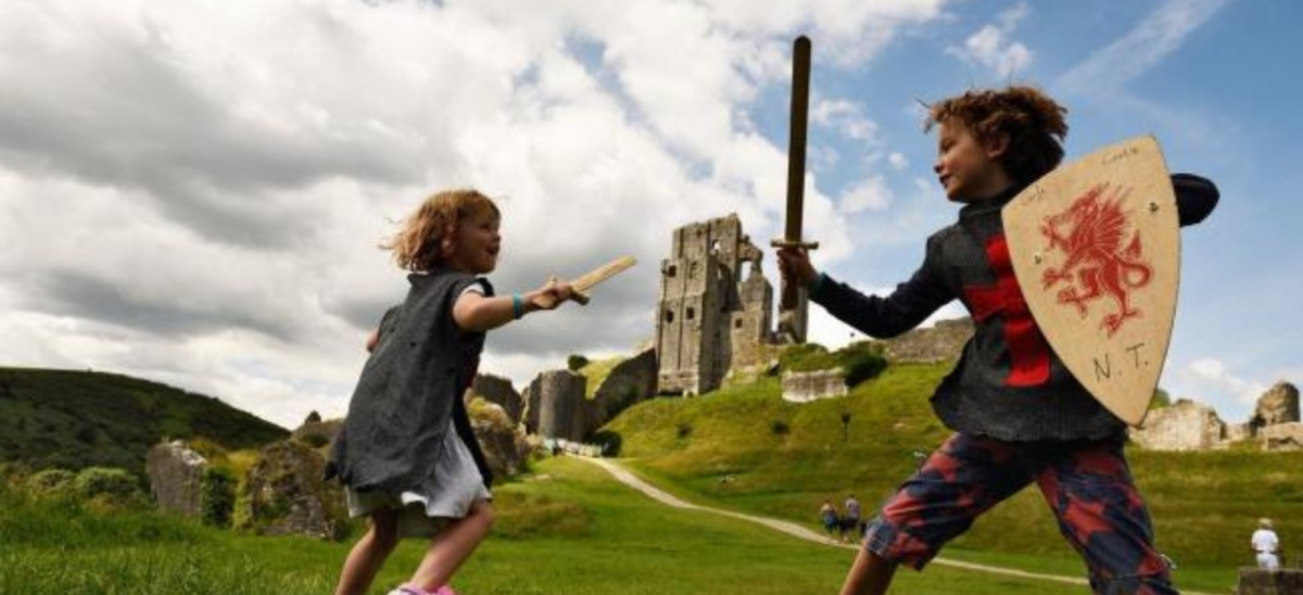 Two kids playing with swords in front of Corfe Castle