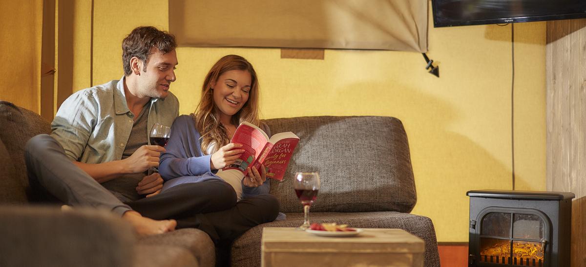 Couple drinking wine on a sofa in a glamping tent