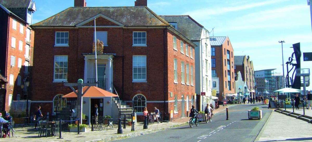 Three cyclists passing the Custom House restaurant on Poole Quay in Dorset