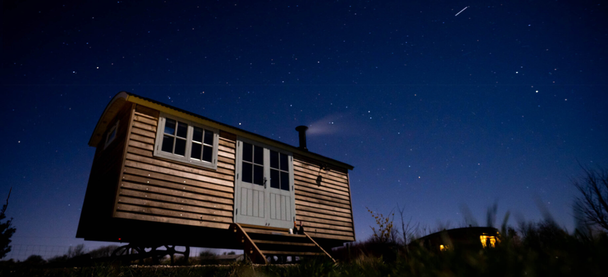 A shepherds hut with night sky and shooting star behind it