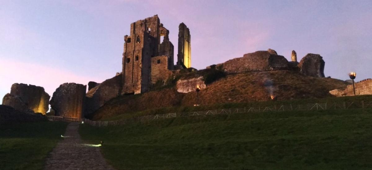 A pink sky blooms as the sun sets behind the romantic ruins of Corfe Castle in Dorset
