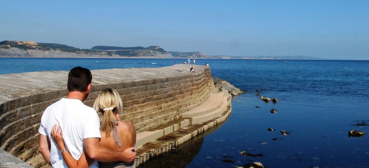 A couple looking towards The Cobb at Lyme Regis with stunning views along Dorset's coast