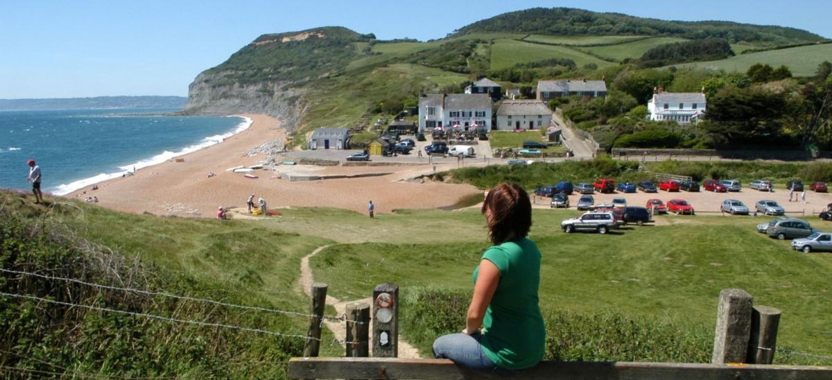 Woman sitting on wooden stile overlooking Seatown beach in Dorset