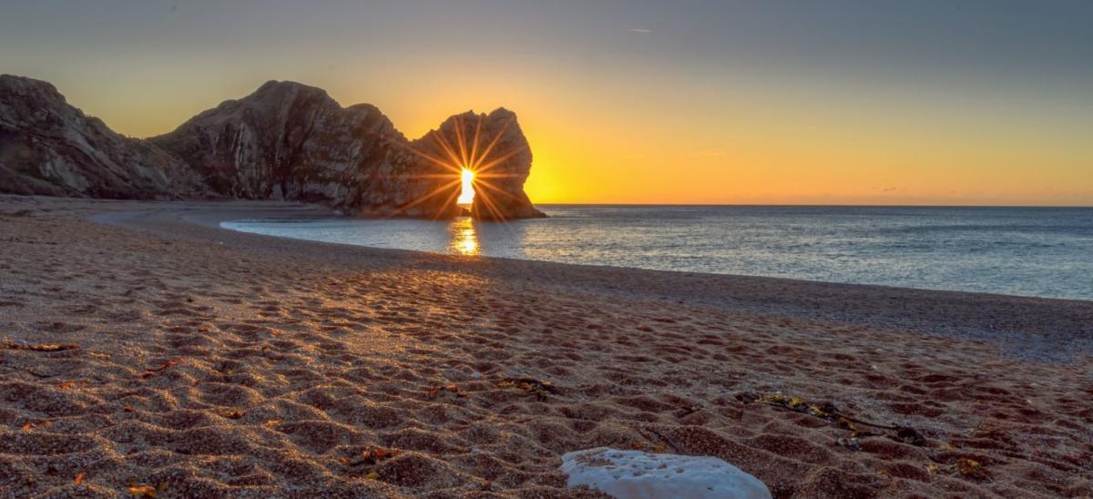 A glorious sight of the sun rising in winter through the arc of Durdle Door on the Lulworth Estate in Dorset. Copyright Steve Hogan.