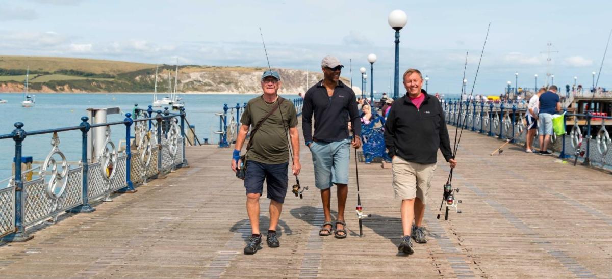 Three men with fishing rods on Swanage Pier in Dorset