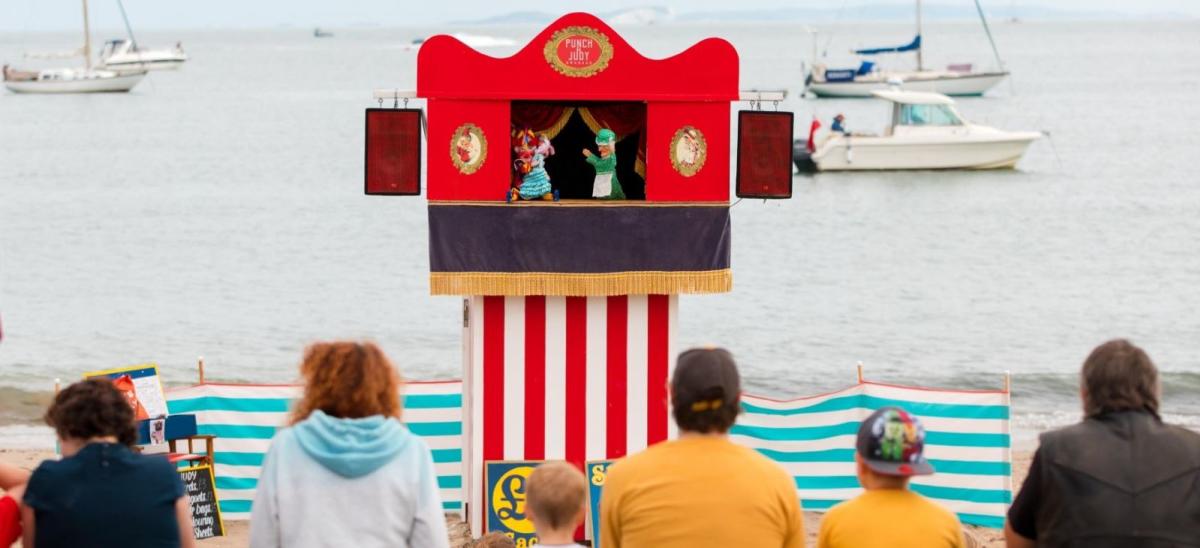 Families watching a traditional Punch and Judy puppet show on Swanage beach in Dorset