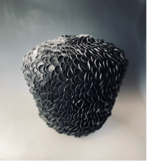 Dark, textured sculpture with overlapping petal-like patterns, creating a layered appearance.