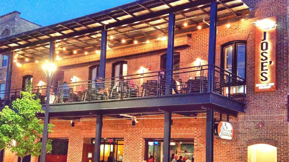 Evening view of Jose’s Blue Sombrero in Milwaukee, with people dining on the upper-level patio under string lights outside the brick building.