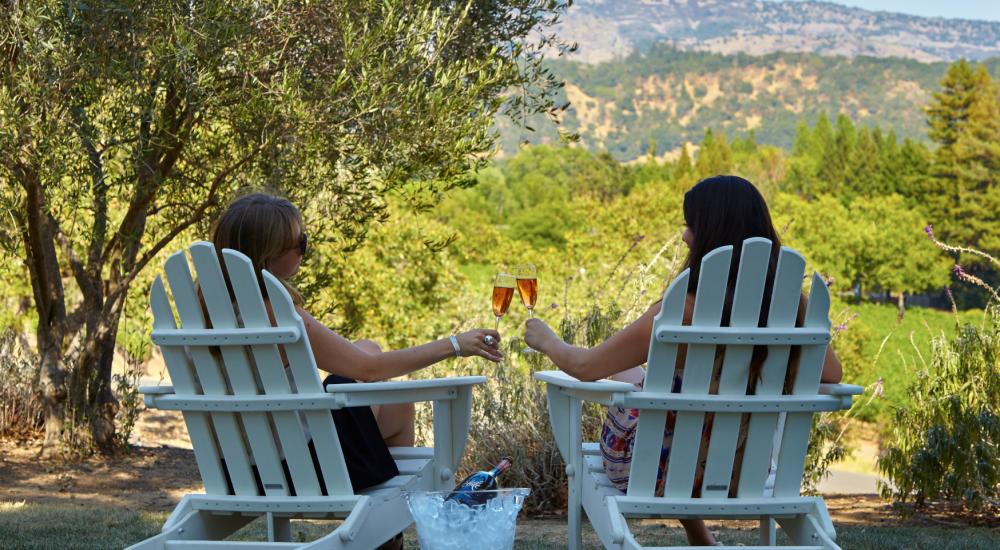 Two women sitting in Adirondack chairs with sparkling wine at the Chandon winery in Napa Valley