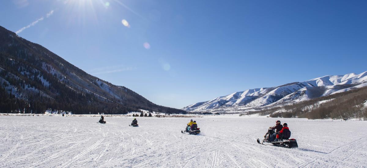Group of snowmobiles in a wide-open field in Weber Canyon on sunny day.