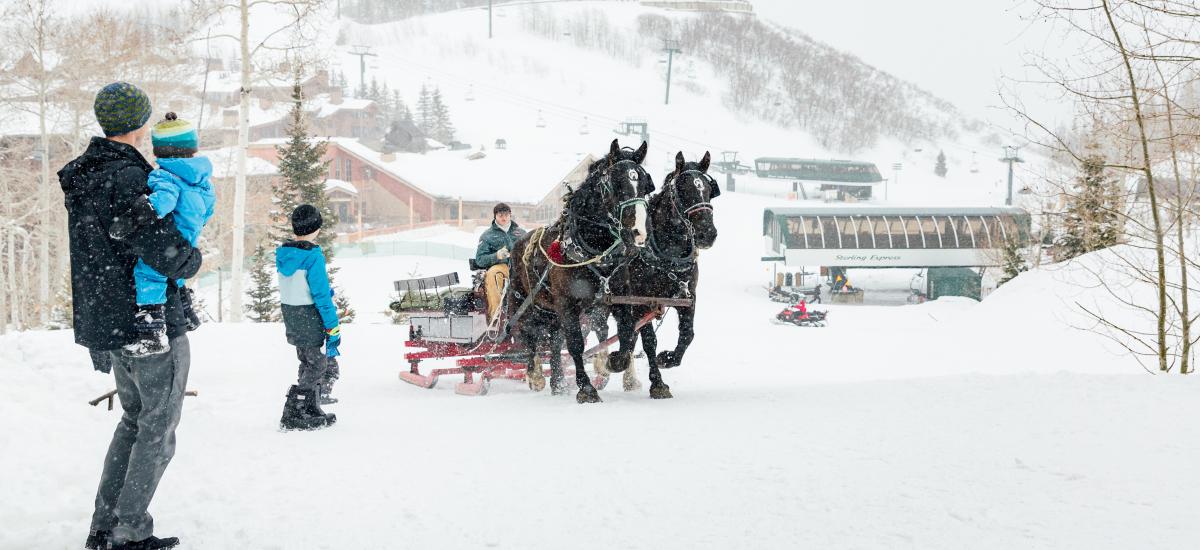 Father and sons waiting outside for sleigh ride on a ski run with snow falling at Deer Valley in Park City, UT