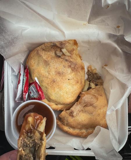 A pasty being dunked into gravy in a to-go box
