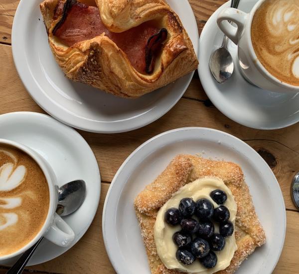 Top-down view of wooden table topped with plates of pastries and foam-art coffees at Fox In the Snow Cafe