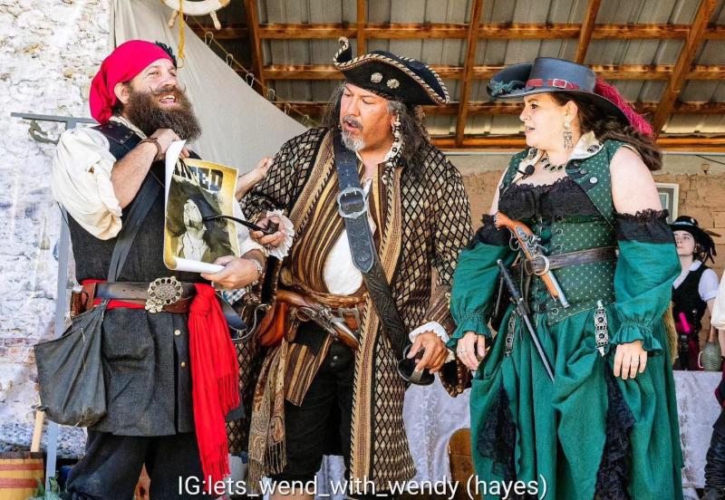 Three people dressed as pirates look at a wanted poster at the Pirate Viking Summer Festival.