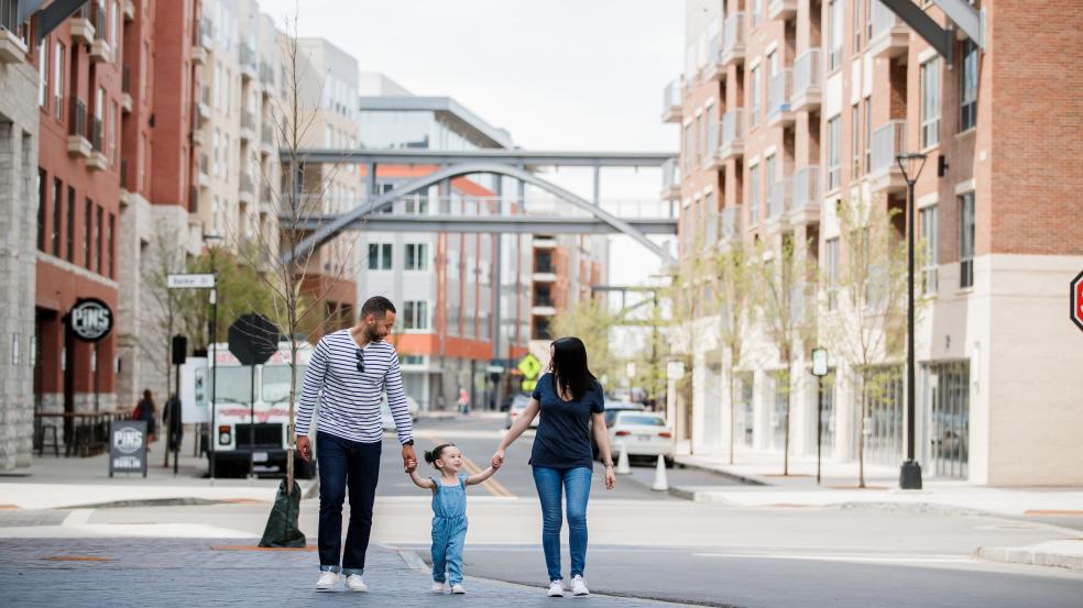 A mom and dad holding handing with their daughter between them in the streets of Bridge Park