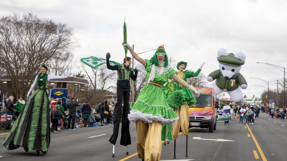 A group of stilt walkers dressed in green performing down the street in the St. Patrick's Day Parade.