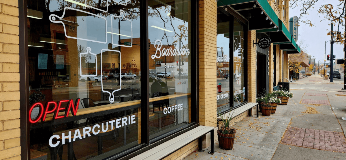 A storefront with a sign that reads "open" and the words "The Boardroom" above it. Snow is on the ground and there is a snowy tree in the background.